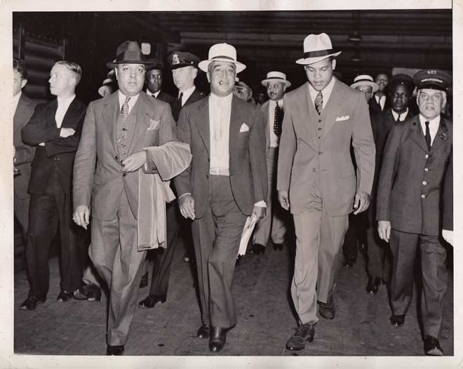 Heavyweight boxer Joe Louis, right, arrives by train in New York on July 5, 1936. Between the champion’s shoulder and the edge of the frame is James H. Williams, Chief and the Grand Central Terminal Red Caps. ACME Press Photo